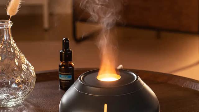 A sleek black essential oil diffuser emits steam and light, accompanied by a glass bottle and a decorative vase.