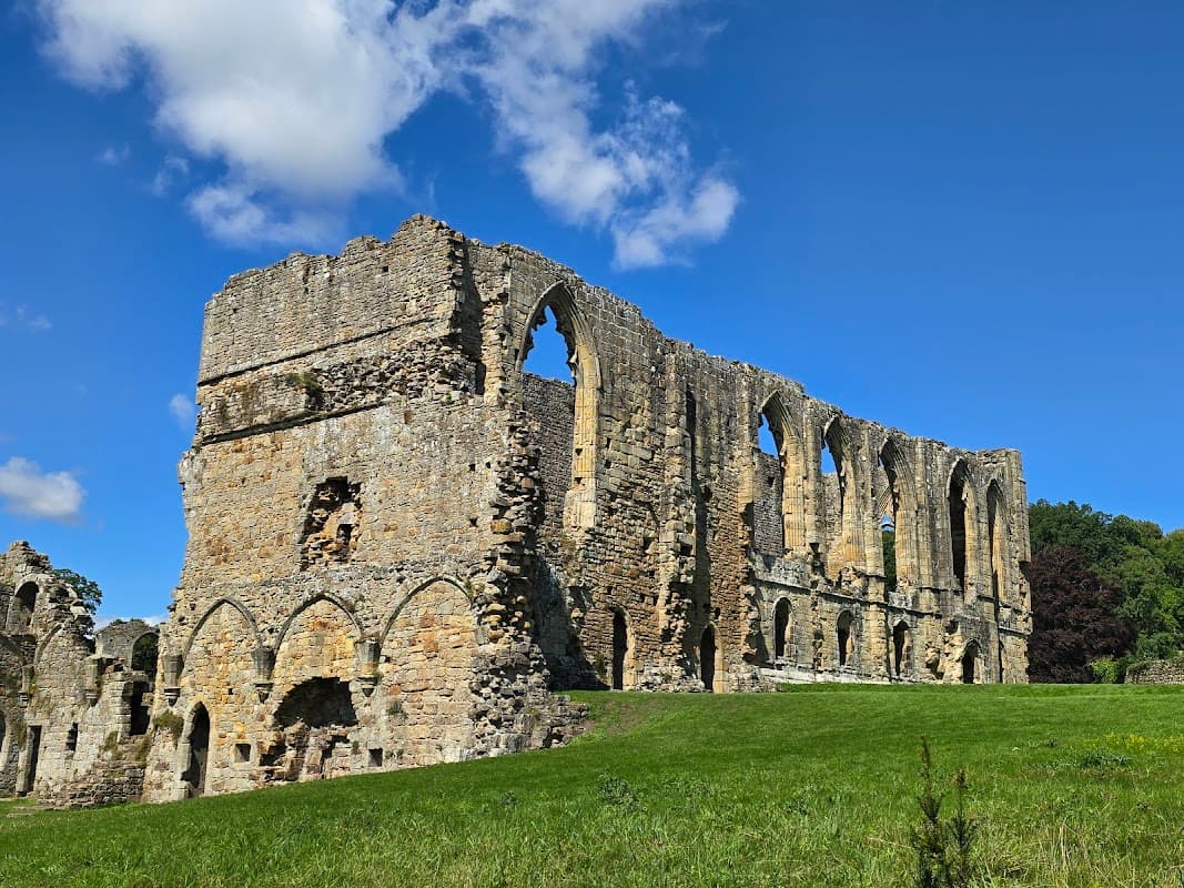 Ruins of St Agatha’s Church with arched windows, surrounded by green grass and blue sky in Easby, Yorkshire.