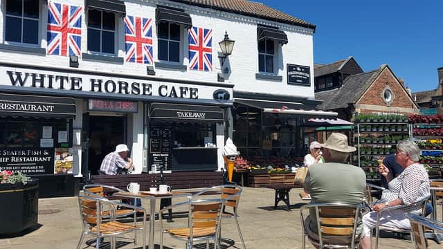 White Horse Cafe with outdoor seating, Union Jack flags, and vibrant flower displays in Thirsk Market Place.