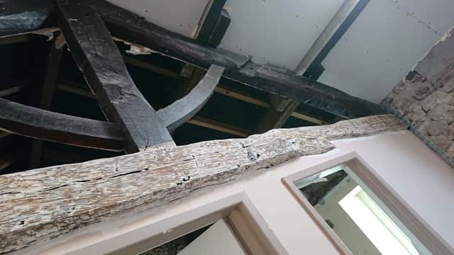 Exposed wooden beams and rustic stone walls in a building under renovation, showcasing historical architectural features.