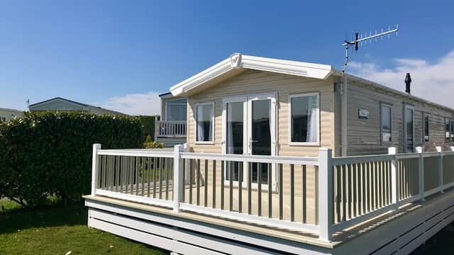 Modern holiday home with a deck, surrounded by green hedges and a clear blue sky at Upwood Holiday Park, Oxenhope.