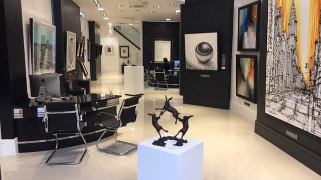 Modern art gallery with sleek black and white decor, featuring sculptures and various framed artworks on display.