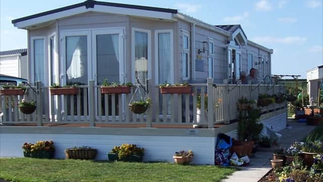 A modern caravan with a deck, surrounded by flower pots and greenery, set against a clear blue sky in Bempton, Yorkshire.
