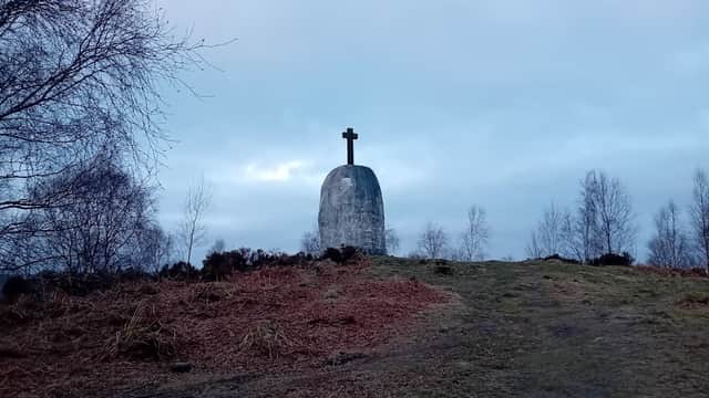 A large stone monument with a cross atop, surrounded by trees and a cloudy sky in Farnhill, Yorkshire.