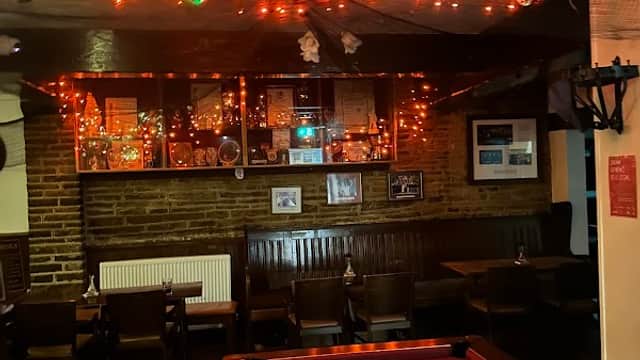 Cozy bar interior with a pool table, warm lighting, and rustic brick walls adorned with framed pictures.