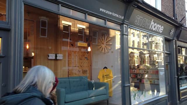 Charming gift shop exterior featuring a large window display with a blue sofa, merchandise, and a yellow shirt.