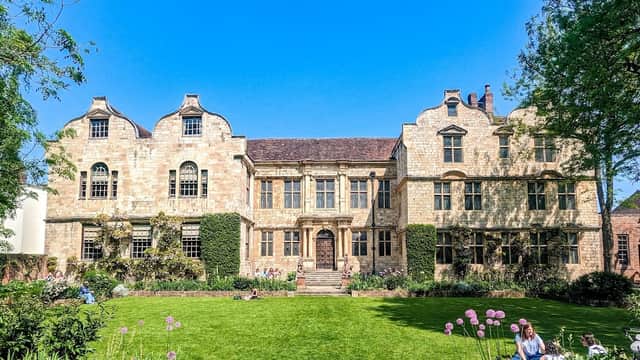 Historic Treasurer's House in York, featuring stone architecture, manicured gardens, and blue sky. Visitors relax on the lawn.