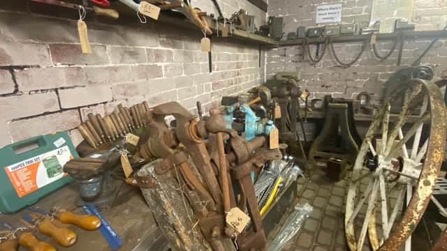 Vintage tools and machinery displayed on wooden shelves in a brick-walled shop, with various items tagged for sale.