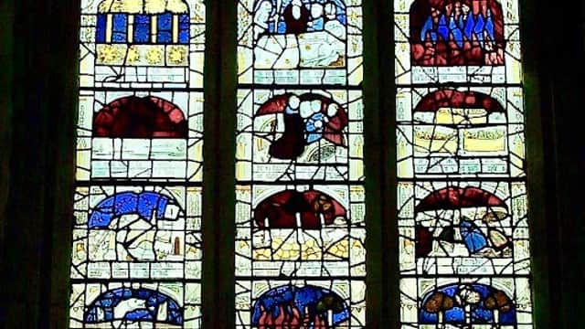 Stained glass window depicting biblical scenes with vibrant colors and intricate designs in a historic church setting.