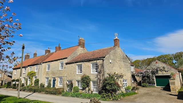 Stone cottages with red roofs, surrounded by greenery, under a clear blue sky in Hovingham, Yorkshire.