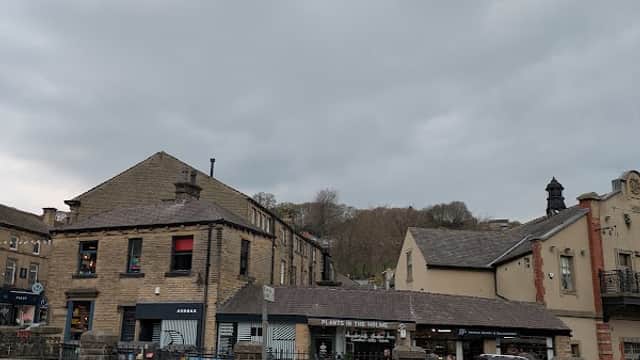 Towngate Car Park in Holme Valley, featuring stone buildings, shops, and a cloudy sky above. Traffic cones in the foreground.