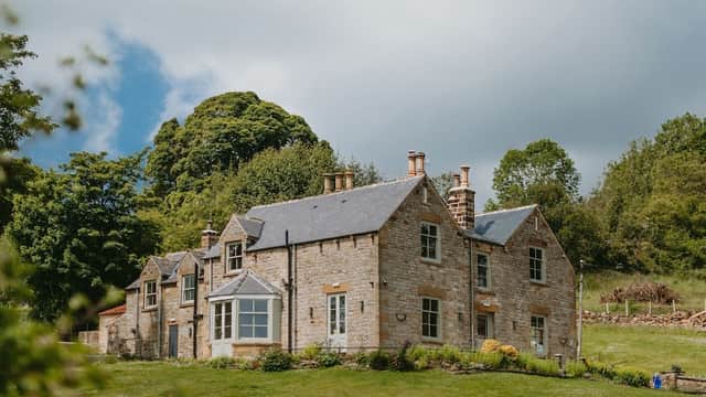 Stone building with multiple windows, surrounded by greenery and trees under a partly cloudy sky.