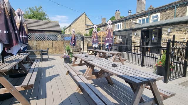 Outdoor seating area with wooden picnic tables, umbrellas, and planters at Pear Tree Bar in Norwood Green, Yorkshire.
