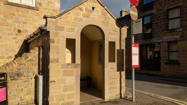 Stone archway entrance with a bench inside, near a bus stop and no entry signs on King Street, Bewerley.
