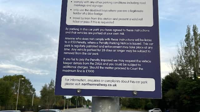 Sign on a pole detailing parking rules for Garforth Station Car Park, with empty parking spaces in the background.