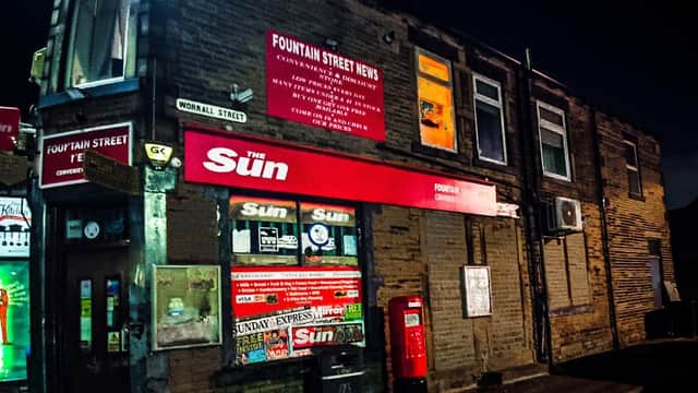 Fountain Street News corner shop at night, featuring a red sign, newspaper displays, and a vintage red phone box.