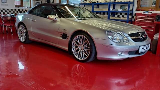 Silver Mercedes sports car parked in a bright red garage with checkered decor and framed automotive artwork.