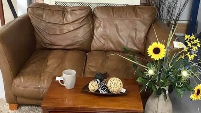Brown leather sofa with a coffee mug, wooden nesting tables, and a vase with sunflowers and decorative items.
