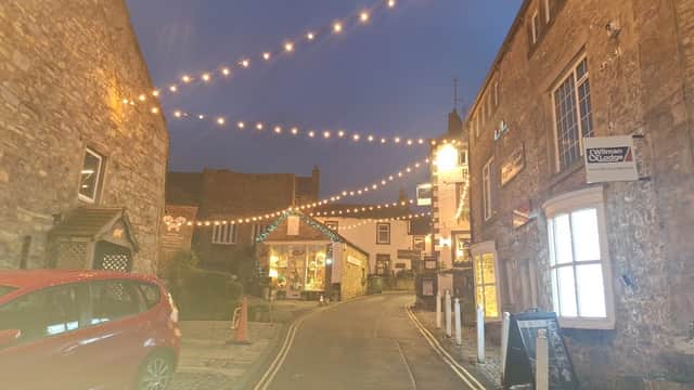 Twinkling lights adorn a charming street in Grassington, with stone buildings and a cozy atmosphere at dusk.