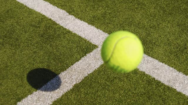 A bright yellow tennis ball bouncing near a white line on a green court surface.
