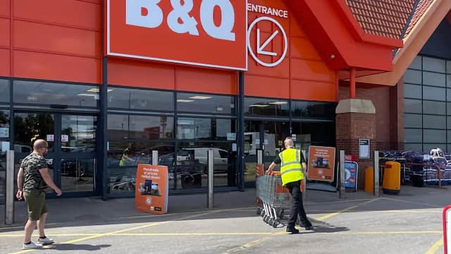 B&Q store entrance with two customers, one pushing a cart, clear blue sky, and red roof architecture.