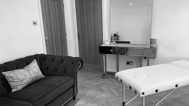 Chic treatment room with a black tufted sofa, mirrored table, and a massage bed on a wooden floor.