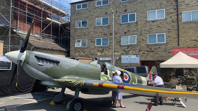 A vintage aircraft displayed in a car park, with nearby scaffolding, buildings, and people interacting around it.