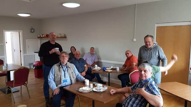 Group of people seated around tables in a community hall, enjoying drinks and snacks. Bright, welcoming interior.