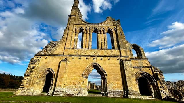 Ruins of Byland Abbey with tall stone walls, arched windows, and a dramatic sky in Newburgh, North Yorkshire.