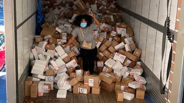 A woman in a mask stands among a large pile of cardboard boxes inside a delivery truck.