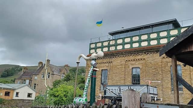 Car park with stone buildings, a flag, and a wooden fence under a cloudy sky in Settle, Yorkshire.
