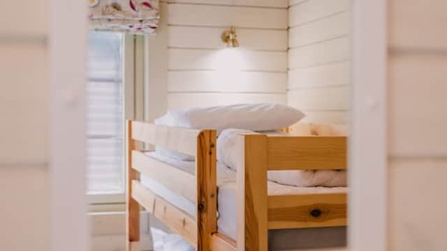 Wooden bunk beds are reflected in a white-framed mirror against a light-colored wall. Natural light enters from a window.