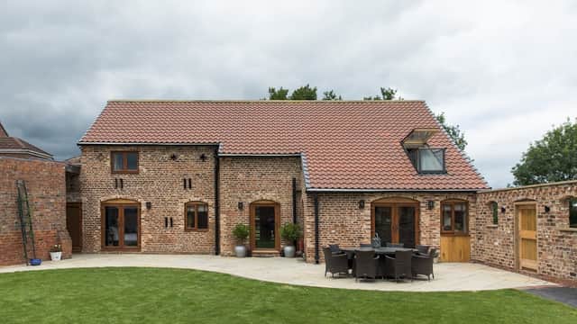 Charming brick barn hotel with a red tiled roof, outdoor seating area, and lush green lawn under a cloudy sky.