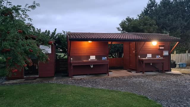 Red wooden utility buildings with lights, surrounded by grass and trees, at Greengate Farm Camping in Kirkbridge, Yorkshire.