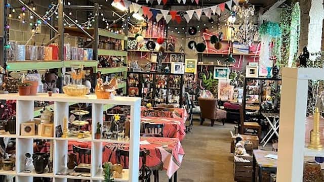 Colorful bunting decorates the ceiling of a cozy shop filled with vintage items and plants, creating a warm atmosphere.