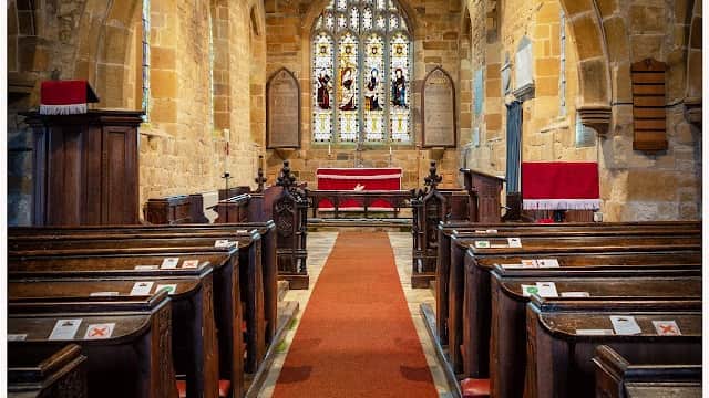 Interior of St Mary the Virgin Church featuring wooden pews, a red carpet, and stained glass windows.
