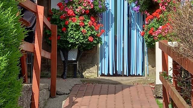 Colorful flower baskets adorn the entrance of Postgate Inn, with a brick path leading to the blue-striped door.