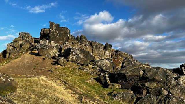 Rocky outcrop at The Wainstones, with a grassy path under a blue sky dotted with clouds in North Yorkshire.
