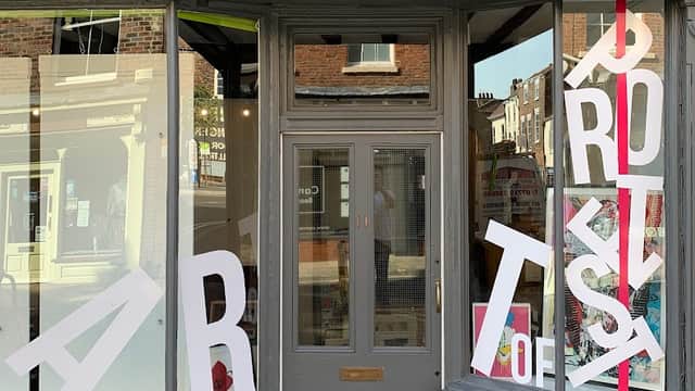 Gallery storefront featuring bold red lettering and large white letters spelling "ART of PROTEST" in the windows.