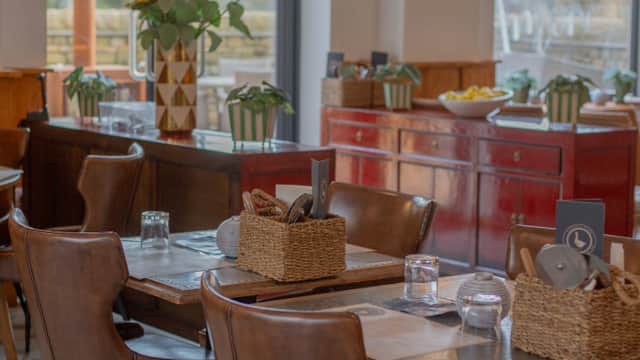 Cozy dining area with wooden tables, wicker baskets, and sunflowers, featuring red cabinets and greenery in a warm atmosphere.