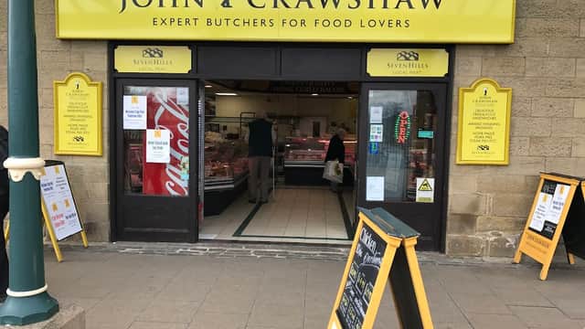 Bright yellow signage for John Crawshaw's Butchers, showcasing meat products, with customers inside and A-frames outside.