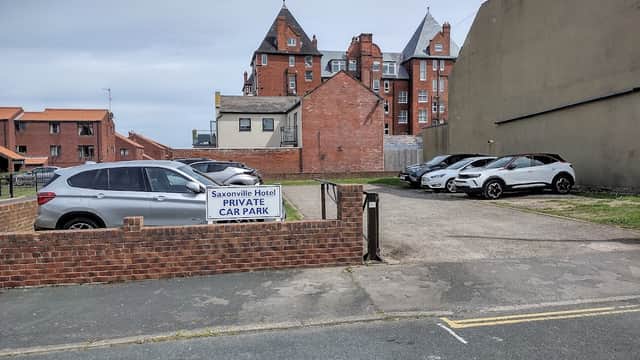 Saxonville Hotel car park with several parked cars and a sign reading "PRIVATE CAR PARK" against a backdrop of buildings.