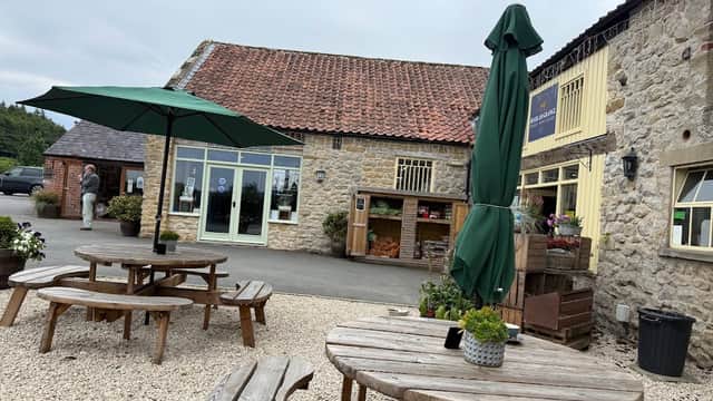 Beadlam Grange Café features outdoor seating with wooden tables, green umbrellas, and a stone building backdrop.