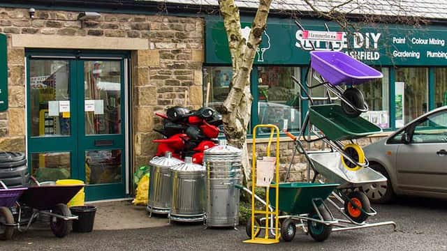 Colorful garden carts and tools are displayed outside Settle DIY shop, with a parked car nearby.