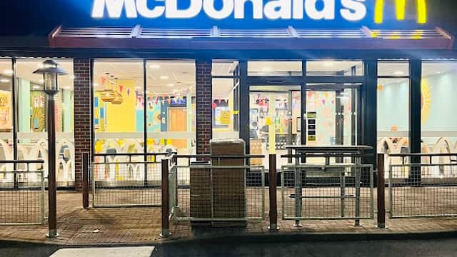 McDonald's restaurant exterior at night, featuring bright signage and large windows with colorful interior decor.