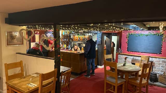 Cozy bar interior with wooden tables, a counter stocked with drinks, and festive lights adorning the ceiling.
