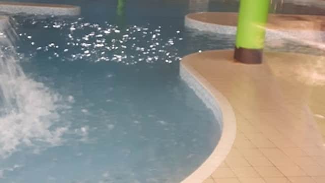 Indoor swimming pool with a splash area, surrounded by colorful murals and green pillars.