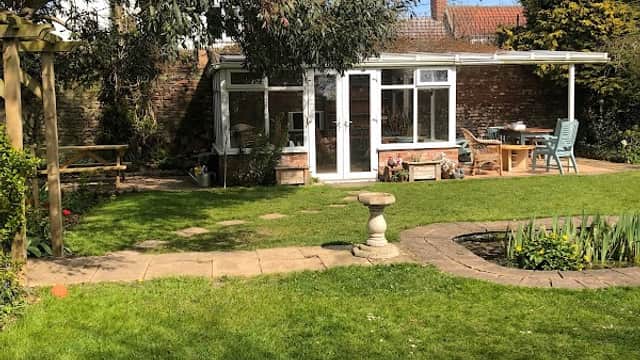 Charming garden at Elm Tree Farm B&B with green lawn, seating area, and a small patio surrounded by trees.