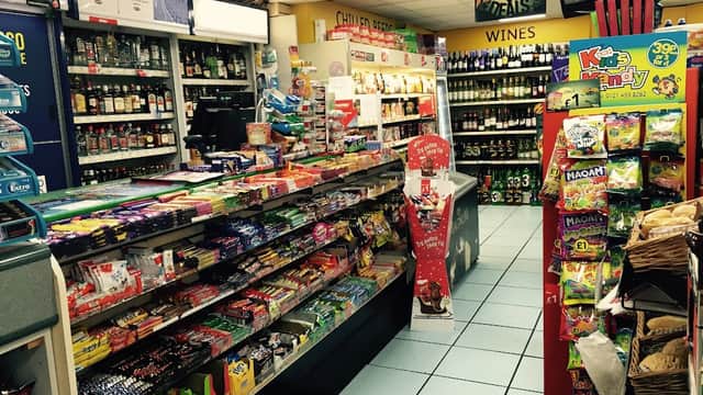 Interior of a convenience store with shelves stocked with snacks, drinks, and wine, featuring colorful candy displays.