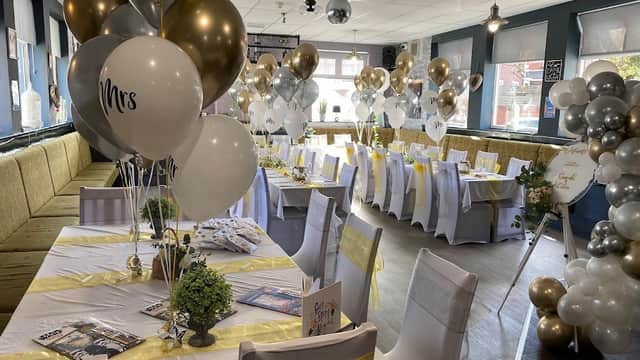 Elegant event setup with white and gold balloons, decorated tables, and chairs in a festive bar setting.
